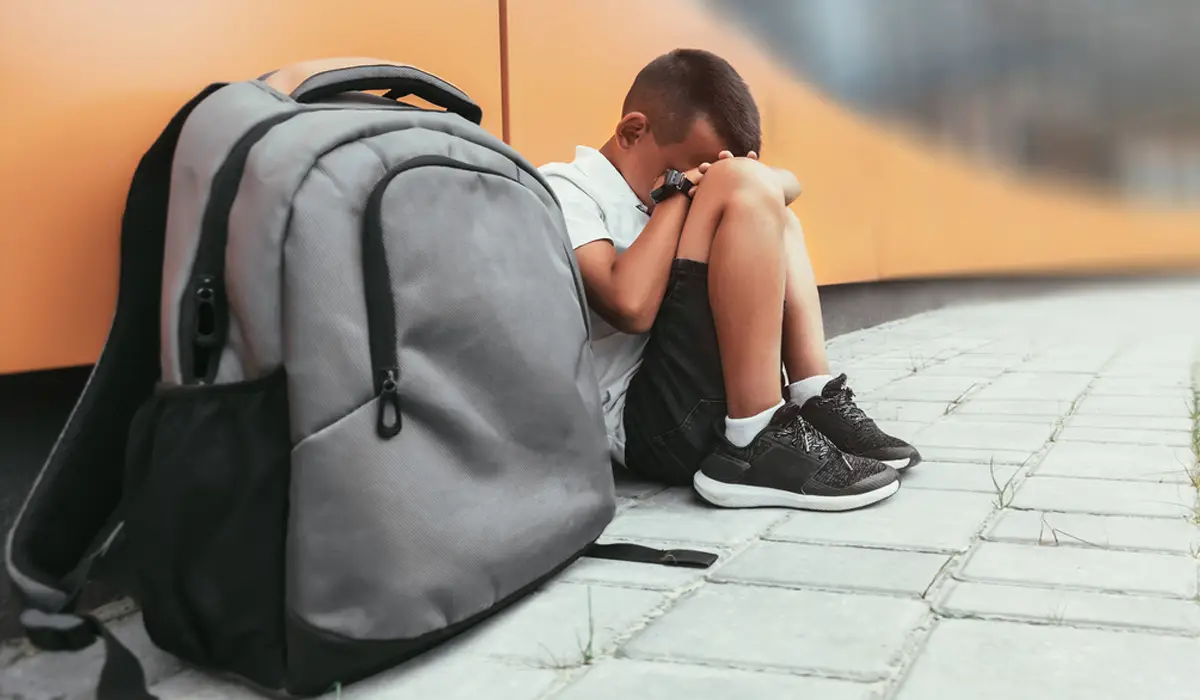 A child crouching in a room with his backpack. Treat childhood anxiety with experts.