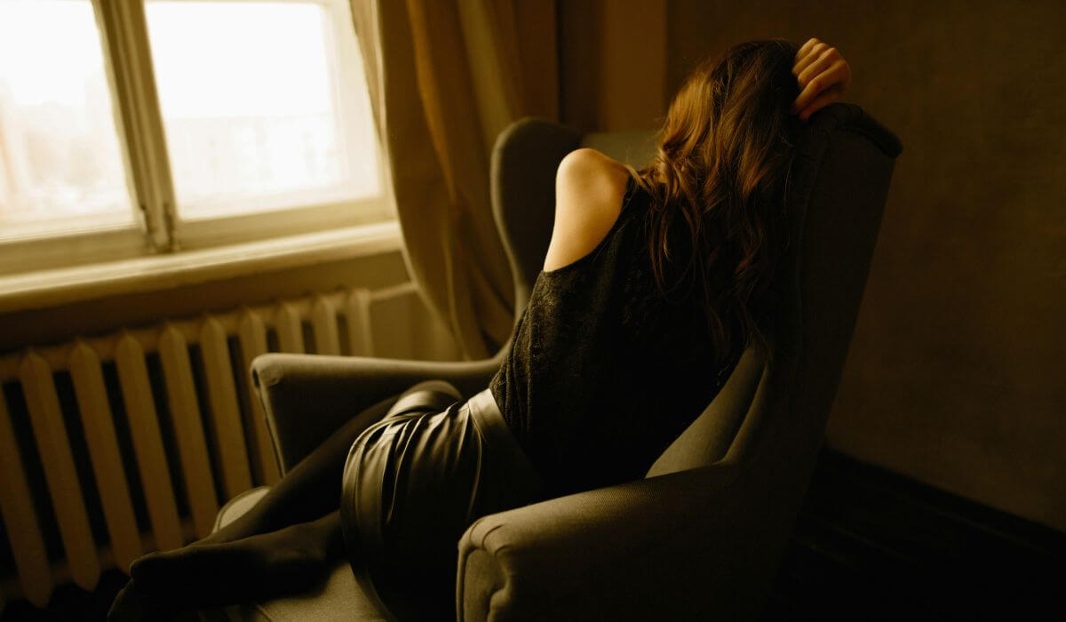 A woman lying on a chair with her face hidden, portraying the emotional exhaustion associated with caregiver burnout and compassion fatigue.