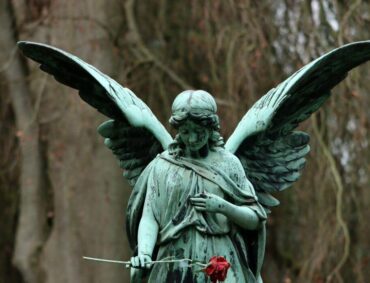 A statue of an angel holding a red rose, representing remembering loved ones after their passing.