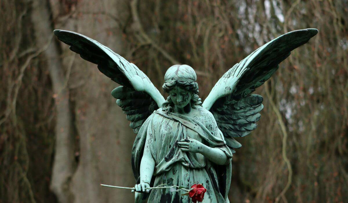 A statue of an angel holding a red rose, representing remembering loved ones after their passing.