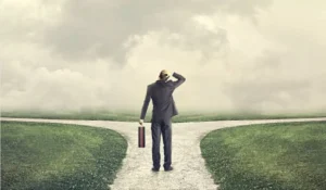 A man standing at a crossroads, symbolizing decision-making and coping with change during life transitions. The foggy background represents uncertainty, while the two paths signify different choices ahead.