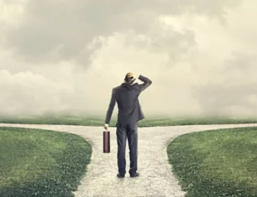 A man standing at a crossroads, symbolizing decision-making and coping with change during life transitions. The foggy background represents uncertainty, while the two paths signify different choices ahead.