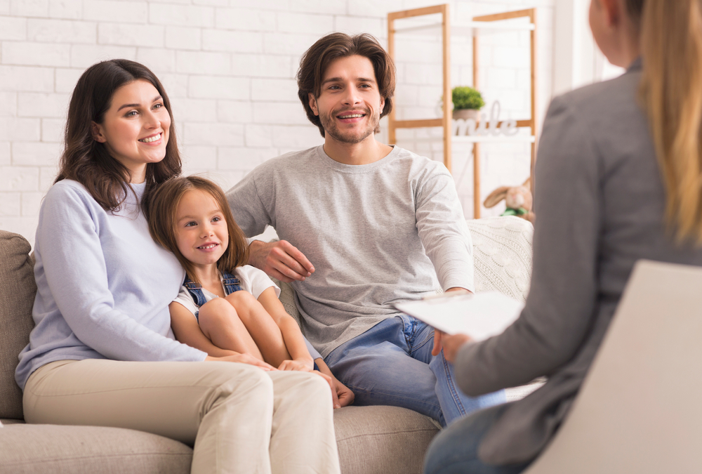 A family engaged in counseling, sitting together on a couch, with a man and woman sharing a supportive moment