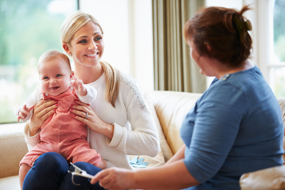 A woman holds a baby while engaging in conversation with another woman, highlighting a moment of parent-child counseling