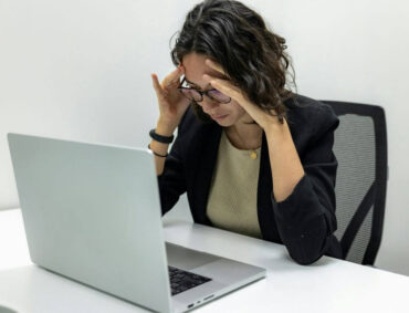 A woman sitting at a desk, holding her forehead in frustration, symbolizing mental health challenges and the need for burnout therapy.