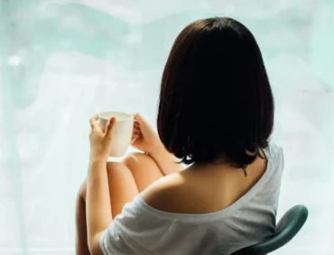 Peaceful woman sipping coffee by the window, focusing on self-care and improving her mental health.