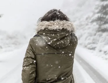 A person in a winter coat walking in snowfall, representing the importance of outdoor activities to manage Seasonal Affective Disorder (SAD).