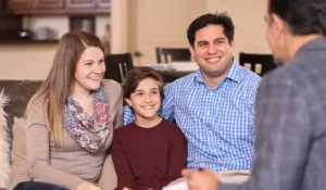 A happy family of three sits on a couch, engaging in an IFS therapy session with a professional counselor.