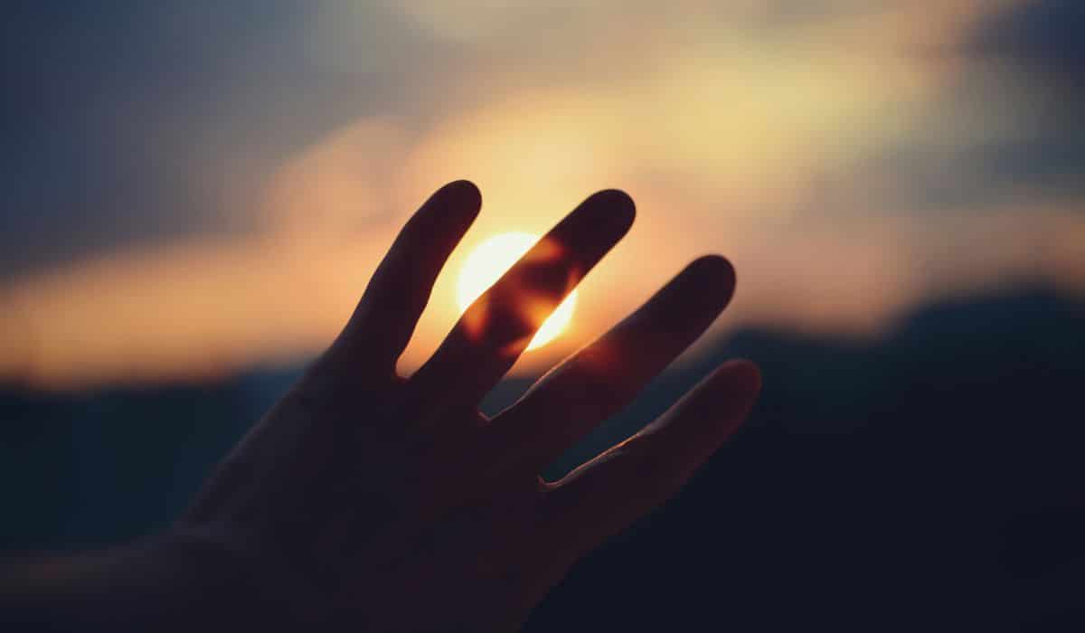 A hand stretches toward sunlight during golden hour, expressing personal healing, hope, and trauma therapy.