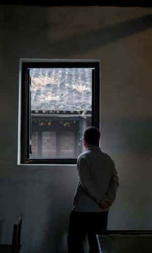 A person stands alone in a dimly lit room, looking out a window—symbolizing inner reflection during trauma therapy.