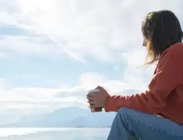 Woman sitting by the water in quiet reflection after IFS therapy.