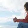 Woman sitting by the water in quiet reflection after IFS therapy.