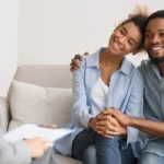 Smiling couple holding hands during supportive couples counseling session focused on building connection and emotional trust.