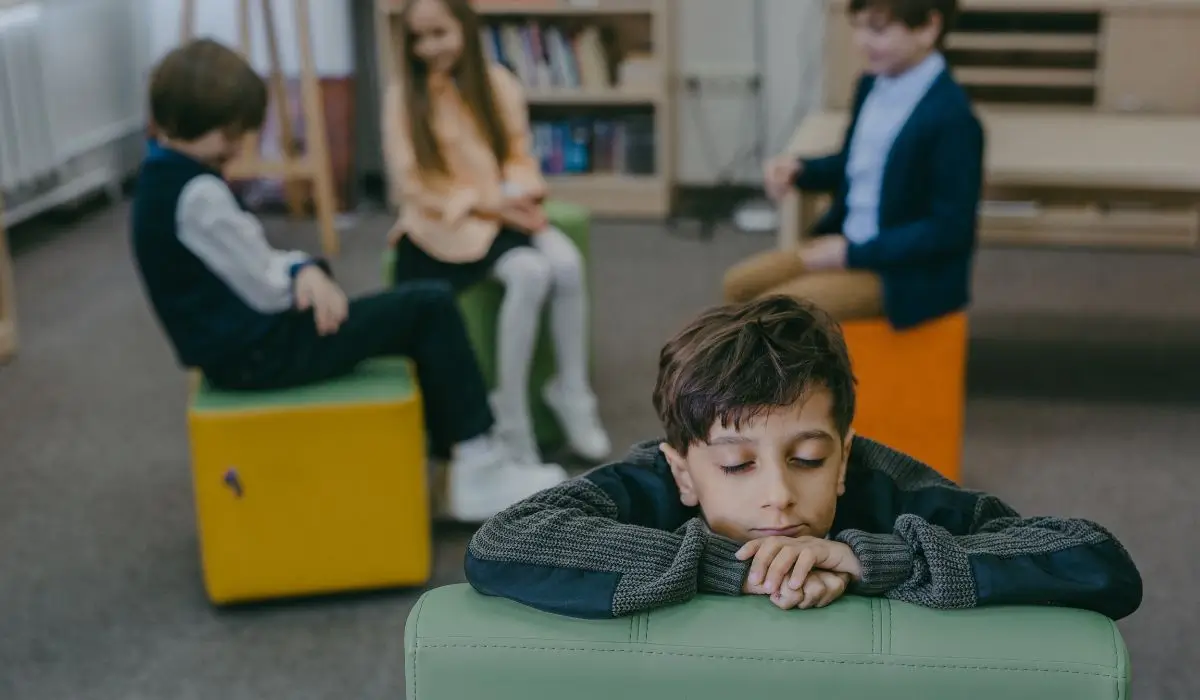 School-aged boy showing signs of childhood anxiety while seated alone during a classroom group activity.