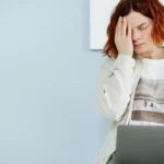 Tired woman with hand on face working at a laptop, illustrating silent depression in high-achieving professionals.